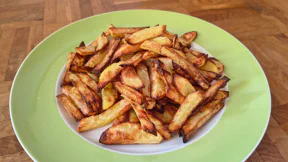 Ein Haufen knuspriger, brauner Pommes liegt auf einem flachen Teller mit grünem Rand. Sie wurden mit Pommesgewürz aus Salz, Curry und Paprikapulver verfeinert.