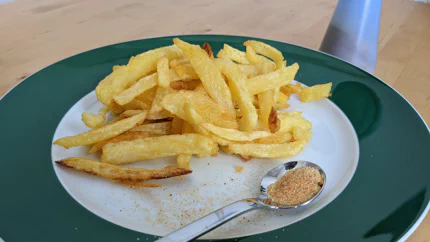 Ein Teelöffeln mit orange-rotem Pizzagewürz auf einem Teller. Daneben liegen selbstgemachte Pommes.