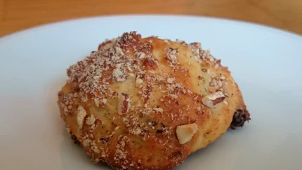 Ein goldbraun gebackenes Quarkbrötchen bestreut mit gehackten Nüssen.