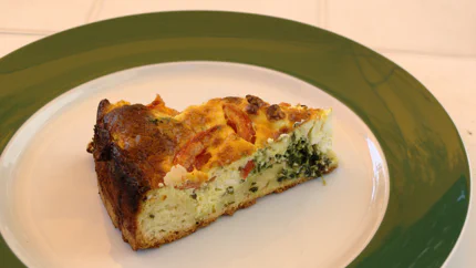 Ein Stück einer Quiche mit Ei, Spinat und Tomaten.