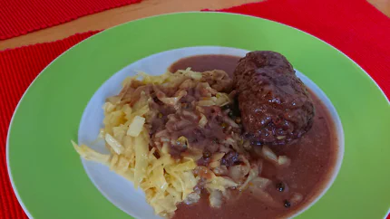 Eine Rinderroulade in dicken, rotbraunen Bratensauce mit Pfefferkörnern - dazu gibt es Krautsalat.