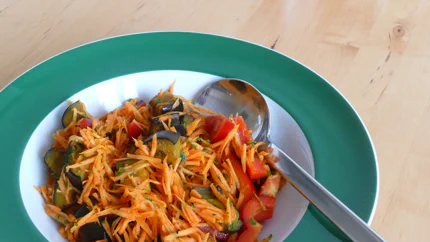 Ein Salat aus geraspelten Rüben, gegrillten Auberginen, Paprika und Petersilie in einem tiefen Teller.