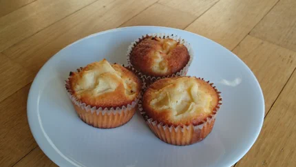 Drei goldgelbe Muffins mit braunem Rand und Fruchtstücken auf einem Teller.