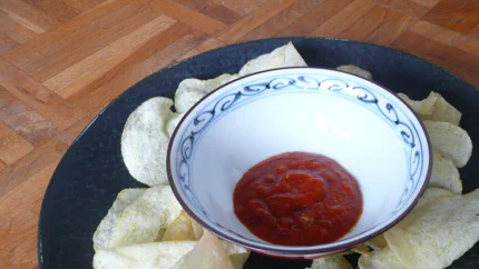 Ein Schälchen mit dickflüssiger, roter Sauce steht auf einem Teller, umgeben von Kartoffelchips.