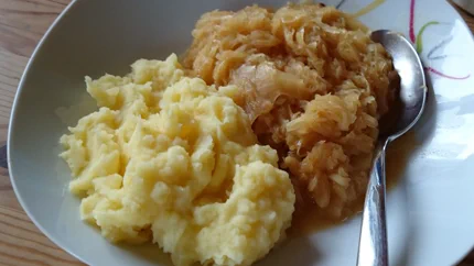 Eine Portion Sauerktraut in rotbrauner Sauce liegt neben einer Portion Kartoffelbrei in einem tiefen Teller. Es liegt ein Löffel neben dem Sauerkraut.