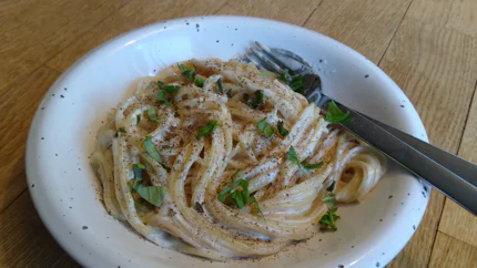 Eine Portion Spaghetti mit einer dicken Sauce aus Schafskäse, Olivenöl, Knoblauch und Basilikum in einem tiefen Teller. Es ist reichlich Peffer darauf.