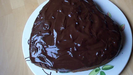 Ein dunkelbrauner, herzförmiger Schokoladenkuchen mit einem glänzenden Guss aus Schokolade.