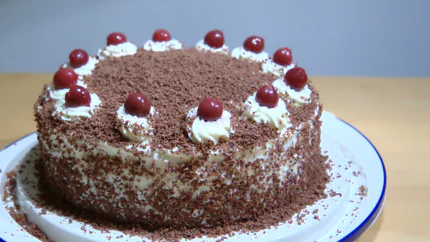 Eine Torte aus mehreren Schichten Biskuitteig, steifer Sahne garniert mit ganzen Kirschen und gehobelter Schokolade.
