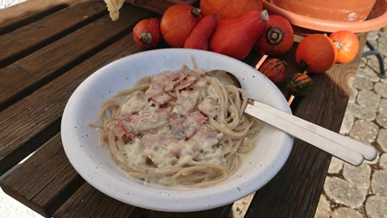 Eine Portion Spaghetti in einer Sahnesauce mit Speck und Pfeffer in einem tiefen Teller auf einem Tisch im Garten.