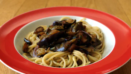 Eine Portion Spaghetti mit gegrillten Auberginen und Zucchini in einem tiefen Teller auf einem Holztisch.