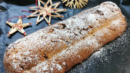 Ein mit Puderzucker garnierter Stollen, in den Rosinen eingearbeitet sind. Er liegt auf einem Backblech vor Weihnachtsdekoration.