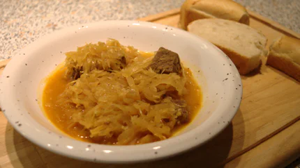 Eine Portion Gulasch aus Rindfleischstücken und Sauerkraut in einer Suppe mit Paprika in einem tiefen Teller. Dazu gibt es Brot.