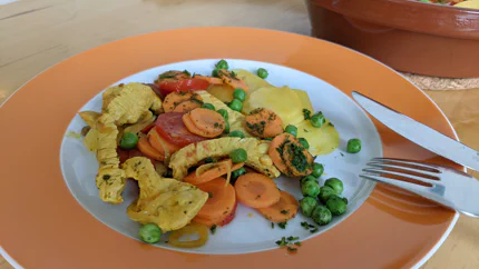 Streifen Hähnchenfleisch, die vom Kurkuma und Curry gelb geworden sind, liegen neben Rüben, Tomaten, Kartoffeln und Erbsen auf einem Teller. Dazu gibt es eine würzige Sauce.