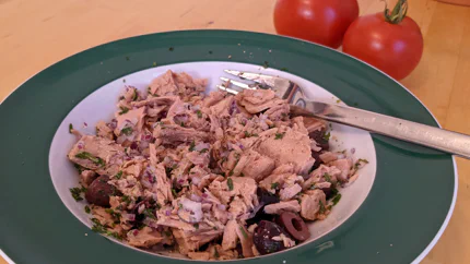 Eine Portion Salat aus gekochtem Thunfischfilet, gewürfelter Zwiebel, Olivenscheiben und Zitronensaft. Dazu gibt es rote, reife Tomaten.