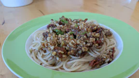Eine Portion Spaghetti mit Pesto aus groben Tomaten- und Walnussstücken und Petersilie in einem tiefen Teller auf einem Holztisch.
