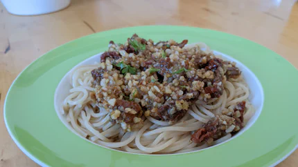 Eine Portion Spaghetti mit Pesto aus groben Tomaten- und Walnussstücken und Petersilie in einem tiefen Teller auf einem Holztisch.