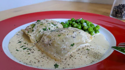 Zwei Maultaschen liegen in einer sahnigen Sauce mit Whisky, Pfeffer und Petersilie. Dazu gibt es Erbsen.