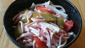 Eine Schale mit Wustsalat aus Lyoner, Gewürzgurken, Gruyère, Tomaten, Essig und Öl.