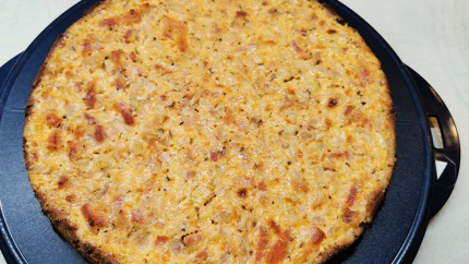 Ein runder Zwiebelkuchen auf einer Tortenform. Oben sieht man viel Kreuzkümmel und braune Stellen vom Backen.