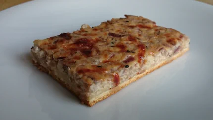 Ein rechteckiges Stück Zwiebelkuchen mit dünnem, knusprigem Hefetig.